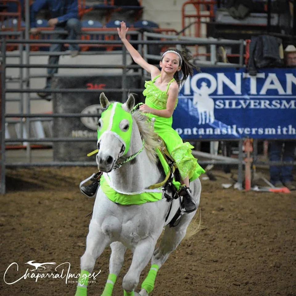 Young Rider Waving on Green-Accented Horse at Rodeo