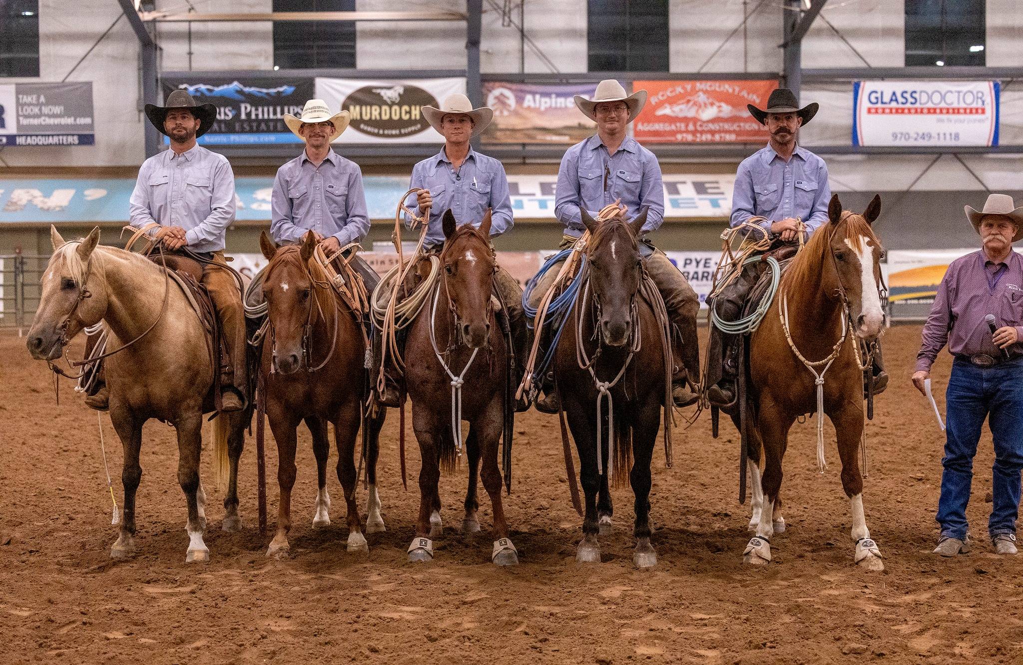 Cowboys and horses posing in an indoor arena with sponsor banners