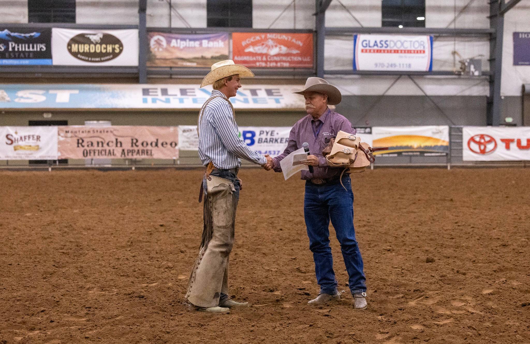 Two Cowboys Shaking Hands at an Indoor Rodeo Event